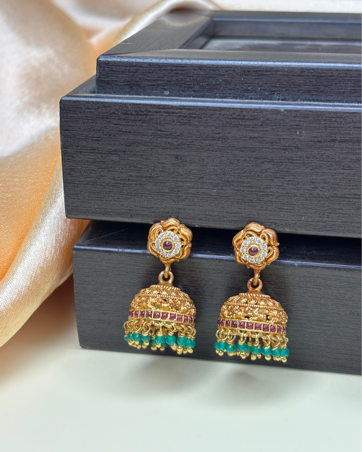 A pair of gold-toned traditional Indian jhumka earrings with red and green stone accents.