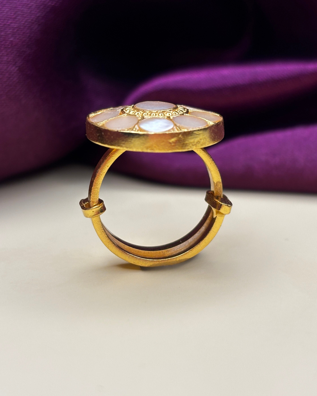 A gold ring with a circular, layered top featuring inlaid white mother-of-pearl.