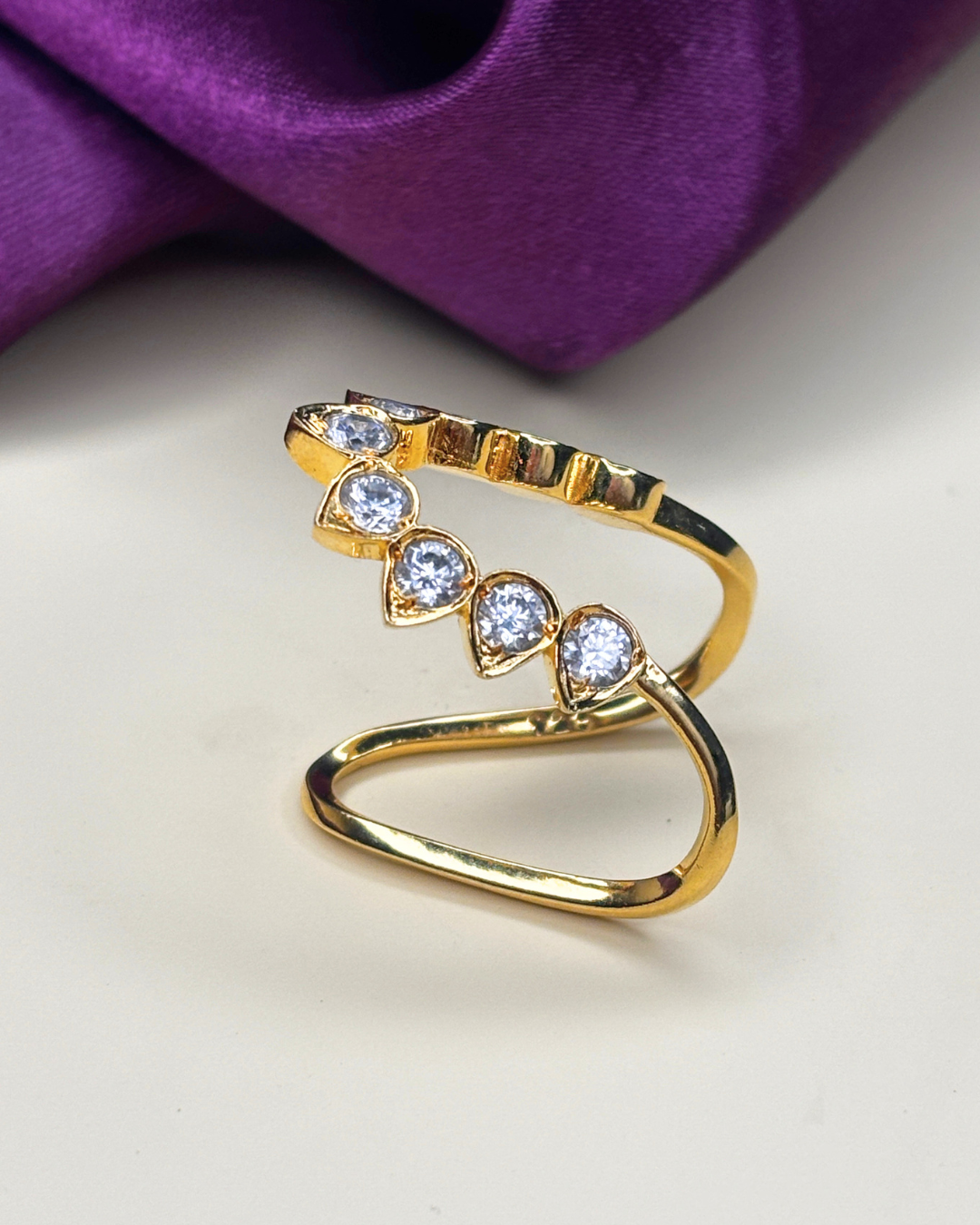 A gold-plated open wrap ring featuring four clear teardrop-shaped gemstones.