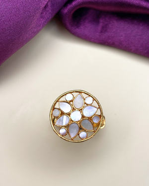 A gold ring with a circular floral pattern of milky white stones.