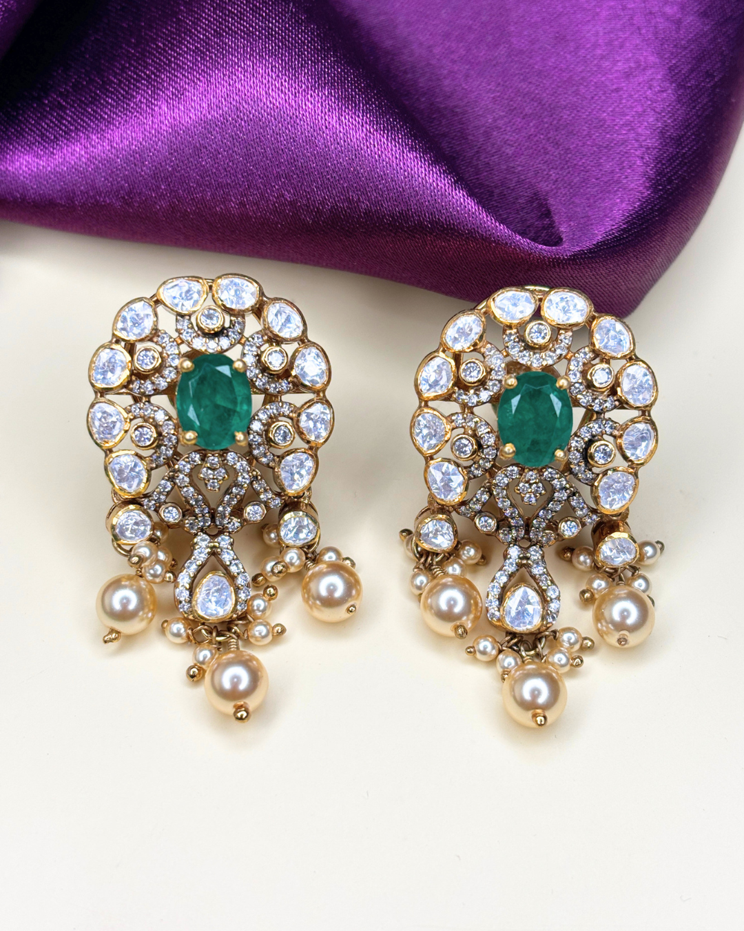 A pair of gold-plated statement earrings featuring oval-cut green emeralds.