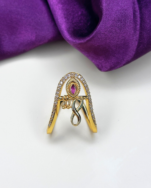 A gold-toned ring designed in the shape of the letter 'A', embellished with clear crystals along the edges and a central teardrop-shaped pink gemstone