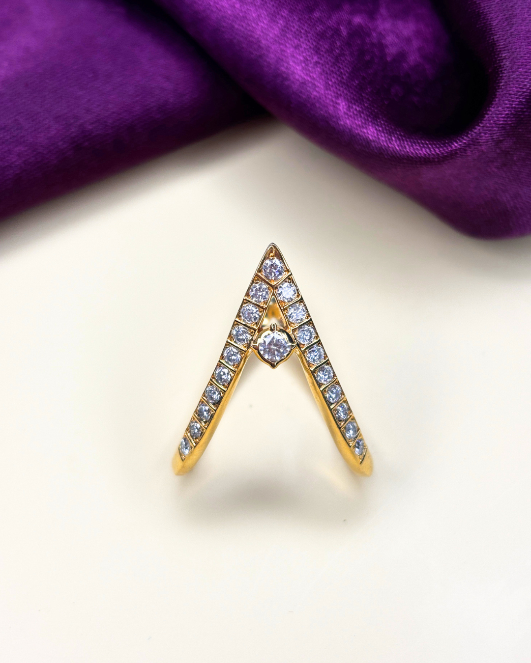 A gold ring designed in a V-shape, adorned with small clear pavé stones and a central round clear stone