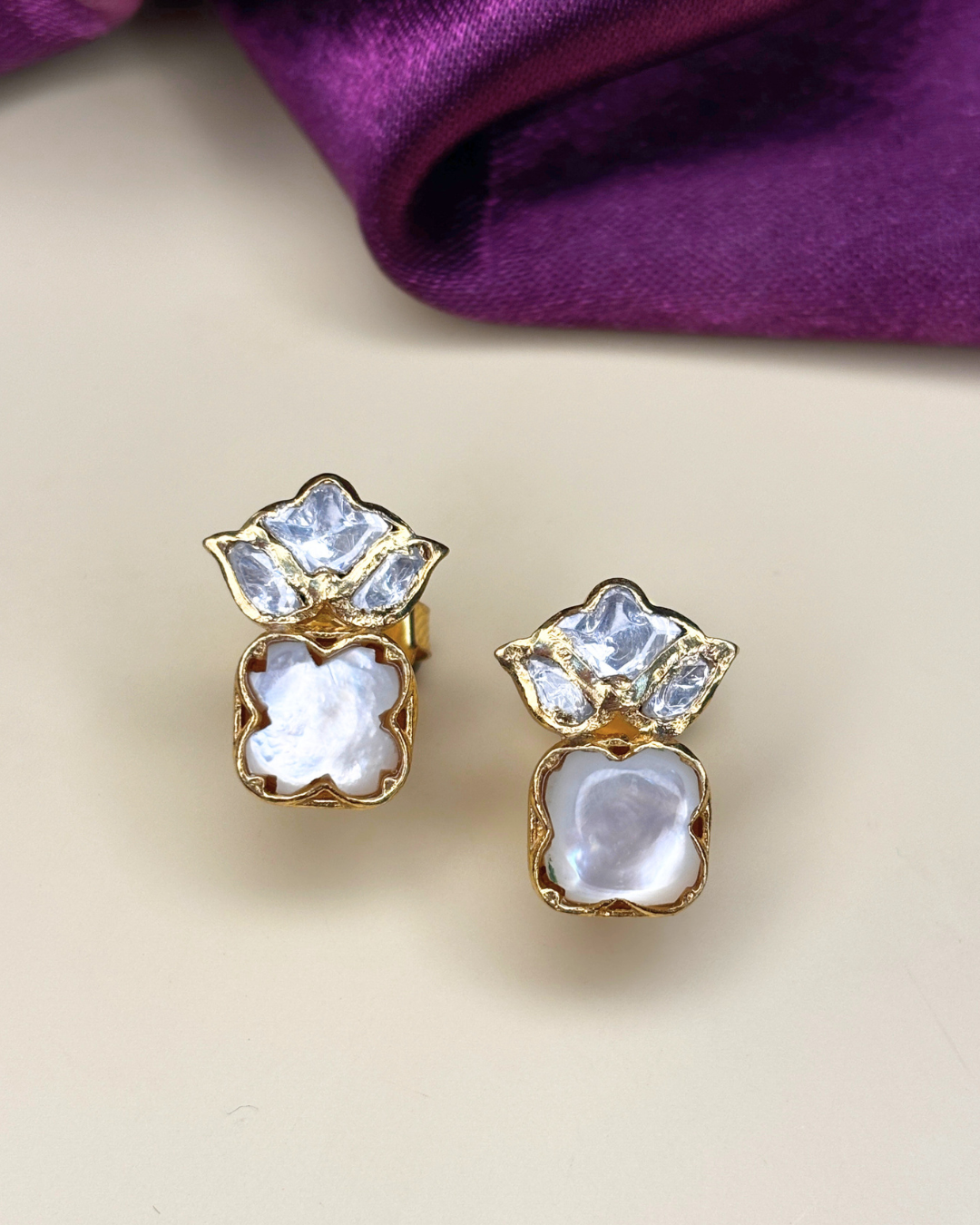 A pair of gold-toned stud earrings with clear rhinestone floral tops and white mother-of-pearl flower-shaped.
