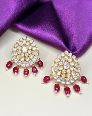 A pair of gold-toned Indian-style earrings adorned with clear crystals and dangling red beads.