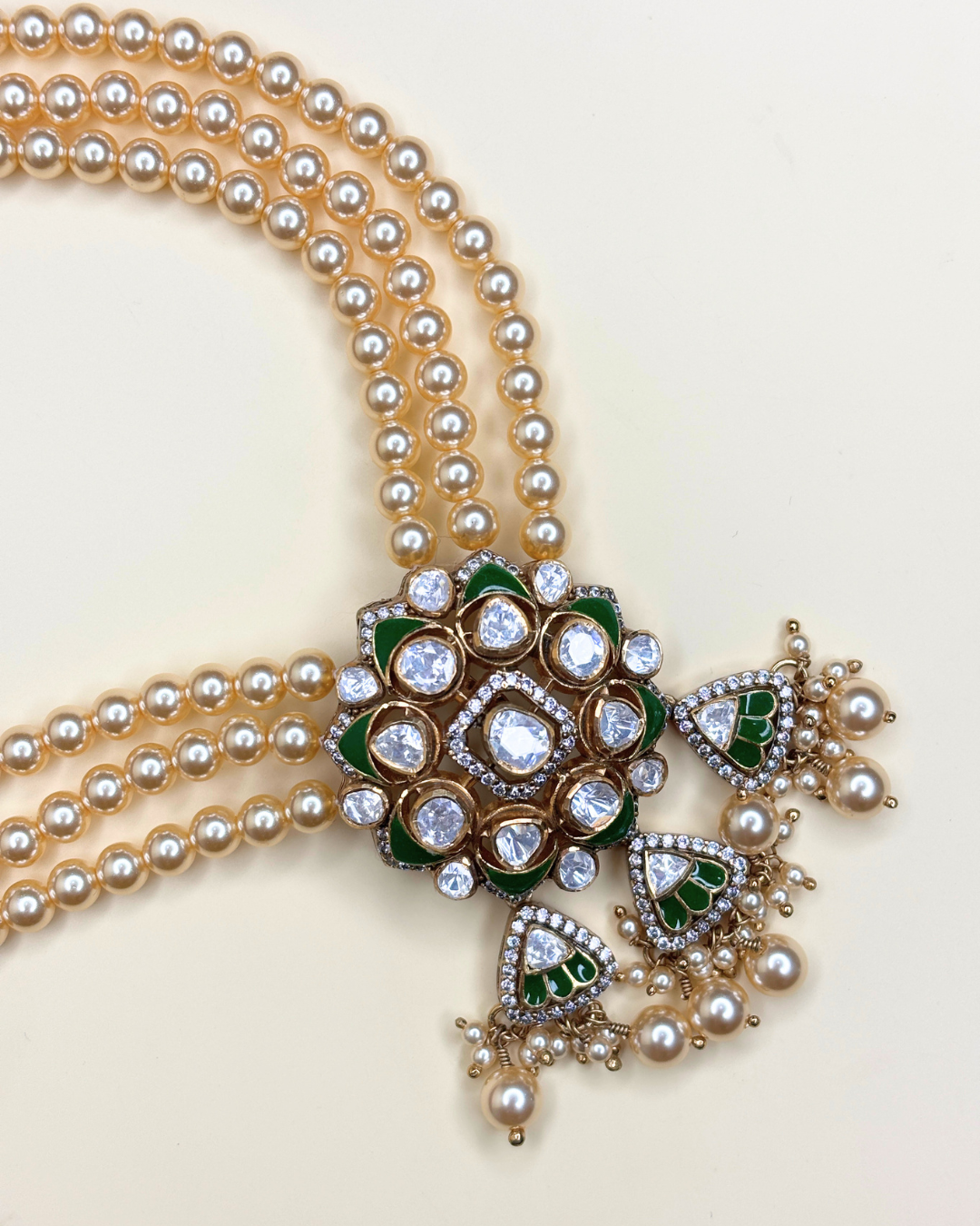 A traditional Indian Kundan necklace with a multi-strand pearl body, a central gold-toned floral cluster adorned with clear stones.