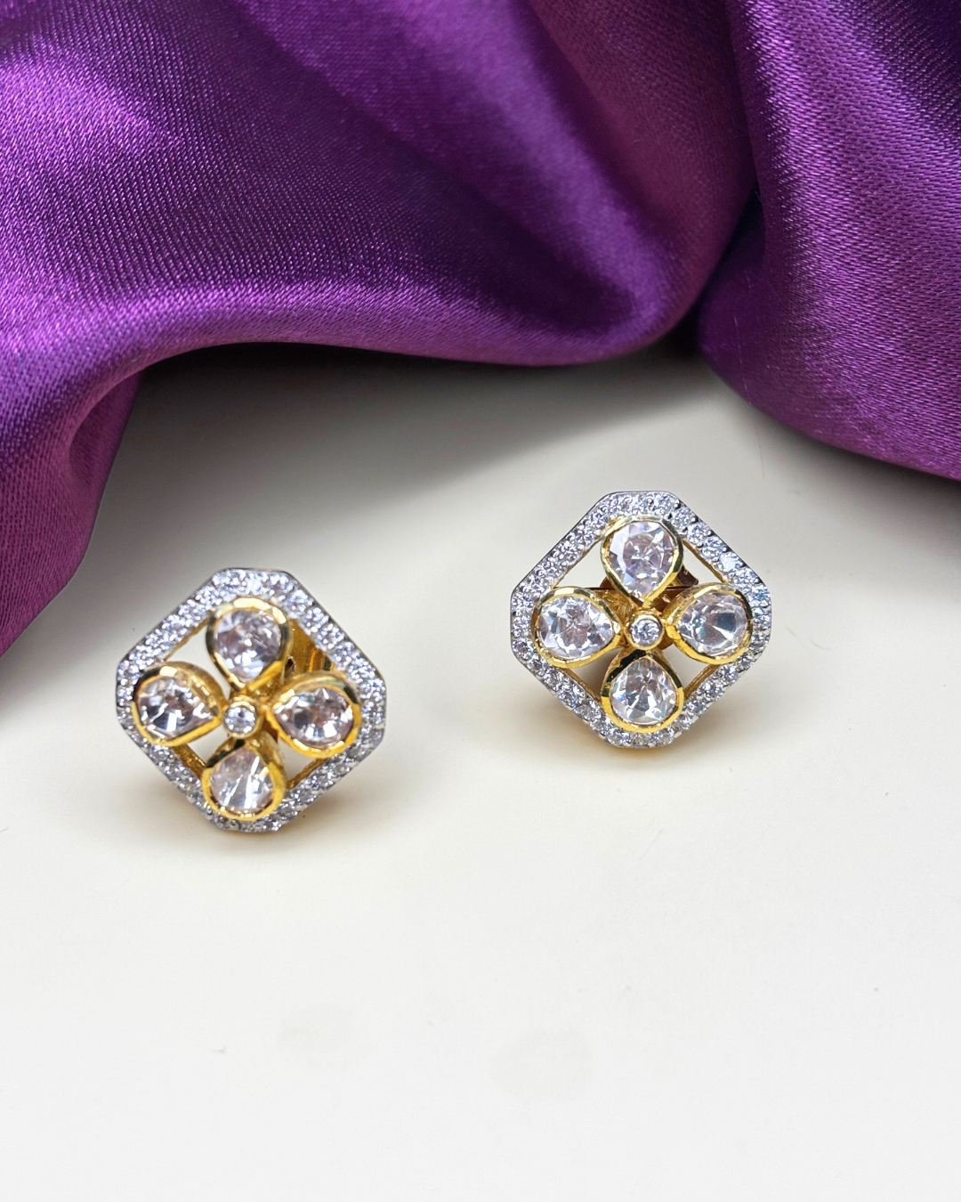 A pair of gold and silver stud earrings with clear teardrop-shaped crystals.