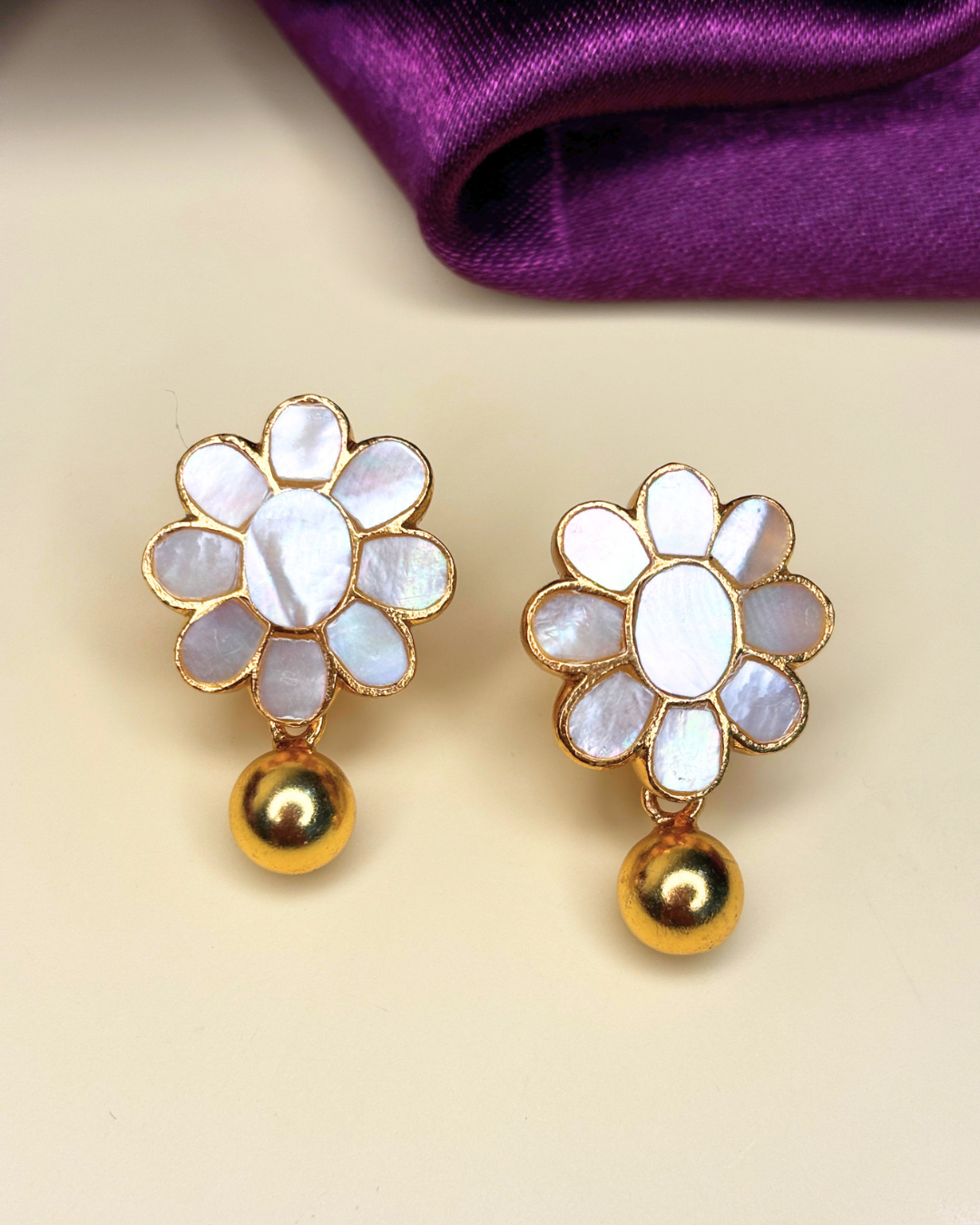 A pair of gold and mother-of-pearl flower-shaped earrings with dangling gold beads.