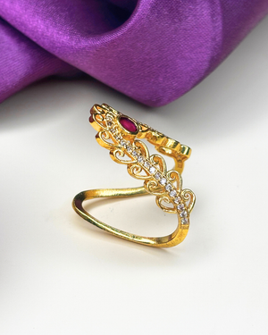 A gold ring designed like a tiara, featuring a small red gemstone.